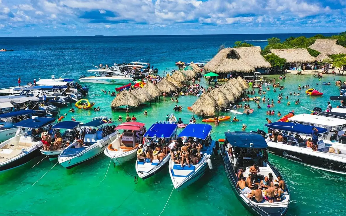 数十艘船并排停泊在浅绿色水中，身后是建在桩上的茅草棚