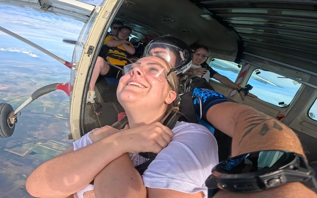 A passenger strapped to her instructor inside the cabin beside the open door